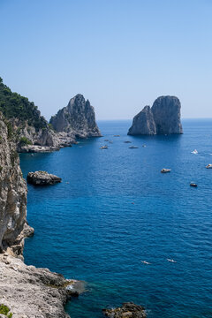 Scenic Coastline View of Faraglioni Rock Formations in Capri, Italy. A panoramic, high-angle view of the iconic Faraglioni sea stacks towering over the deep blue waters of the Mediterranean Sea. The s