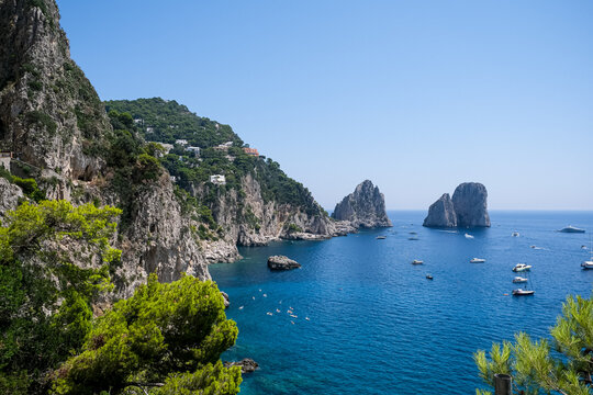 Scenic Coastline View of Faraglioni Rock Formations in Capri, Italy. A panoramic, high-angle view of the iconic Faraglioni sea stacks towering over the deep blue waters of the Mediterranean Sea. The s