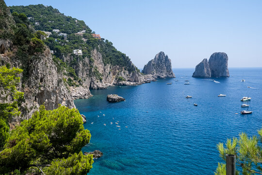 Scenic Coastline View of Faraglioni Rock Formations in Capri, Italy. A panoramic, high-angle view of the iconic Faraglioni sea stacks towering over the deep blue waters of the Mediterranean Sea. The s