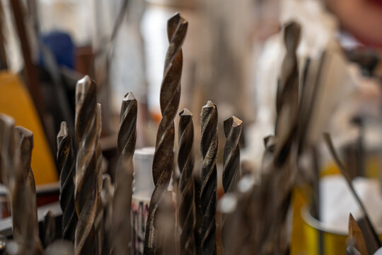Close-up of metal spiral twist drill bits for drilling holes standing vertically in workshop, representing industrial tools, hardware, and metalworking craft.