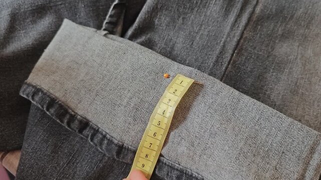 Seamstress measures trousers length with tailor's meter for fitting
