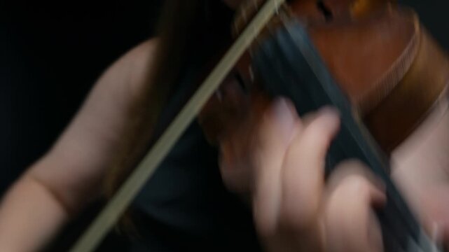 Caucasian young adult female violinist playing classical music on violin in close up. Ideal for music education promos, classical concert advertisements, or artistic documentaries