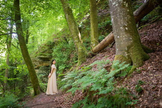art portrait of asian young woman in classic white dress standing in green forest