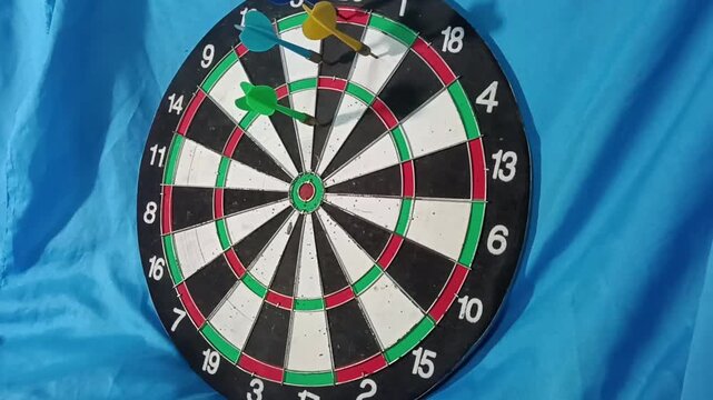 A close-up of a dartboard with several colorful darts stuck in the scoring sections, showing a recreational darts game setup 