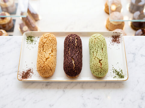 Assortment of three colorful eclair craquelin pastries on a white plate over a marble counter