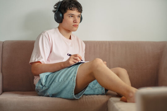 Teenage boy in headphones looking up from his notebook