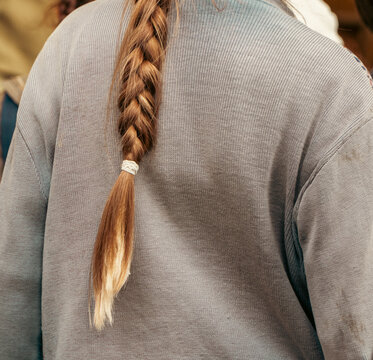 A long woven braid of light brown hair hangs neatly down the back of a woman wearing a grey ribbed sweater.