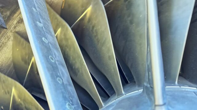 A close look at the blades of a jet engine turbine during maintenance work. The setting is inside an airport hangar. Technicians inspect the engine for safety.