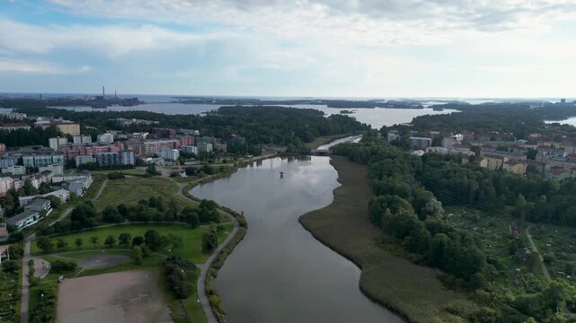Aerial drone view of Pikku-Huopalahden Puisto and the surrounding sea bay in Helsinki, Finland. The image showcases the peaceful waterfront, green park landscape, residential areas.