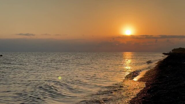 Sunset casts warm hues over Lake Sevan as gentle waves lap against the pebbled shore, creating a tranquil atmosphere in nature