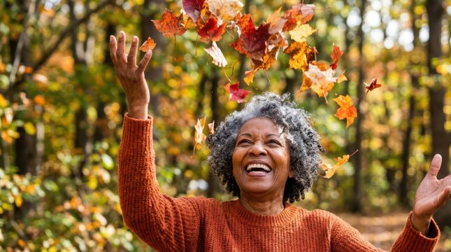 Seniors joyfully spend time outdoors in nature. A joyful senior woman laughs happily while tossing colorful autumn leaves into the air.
