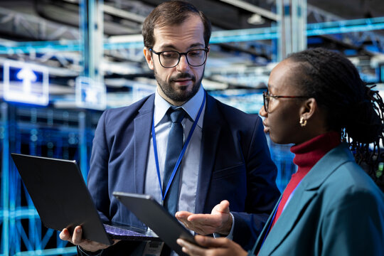 Data center engineering team works together to manage enterprise technology solutions; colleagues use devices to supervise IT operations and infrastructure in a futuristic server room.