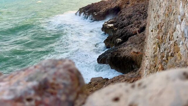 Crashing ocean waves against a rocky coastline with ancient wall