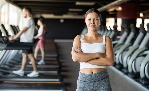 Young athletic woman in sportswear posing near treadmill in gym
