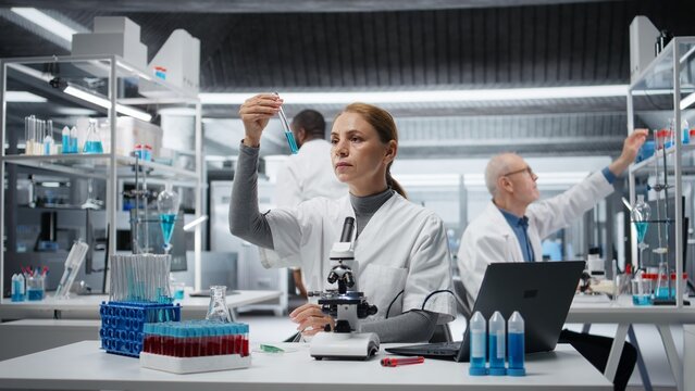 Scientist in lab pipettes blue liquid into a test tube for analysis; laboratory worker transfers a chemical sample to prepare for immediate spectroscopic analysis in the laboratory.