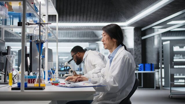 Laboratory technician uses a computer application for DNA data analysis and human health research; Asian lab engineer works with bioinformatics and genomics software on PC for data science.