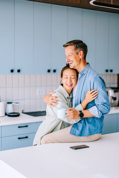 Happy Couple Hugging in Modern Kitchen With Coffee Mug &mdash; Casual Morning Lifestyle and Intimacy