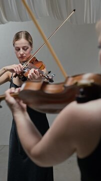 Vertical shot of young adult Caucasian woman playing violin during rehearsal with partner, over shoulder shot. Video is perfect for classical music education or performing arts school promos
