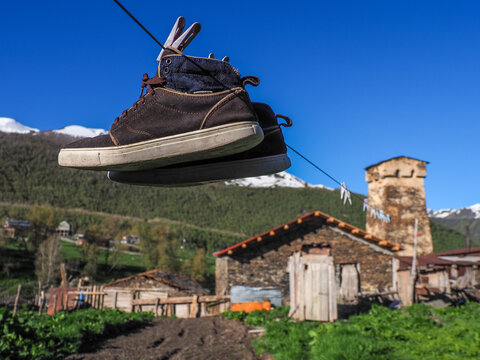 Old Hiking Boots Hanging on a Clothesline in Mestia Village with Traditional Svan Defense Tower and Caucasus Mountains in Svaneti, Georgia
