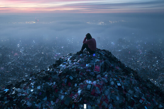 Woman Sitting on Mountain of Electronic Waste Overlooking City