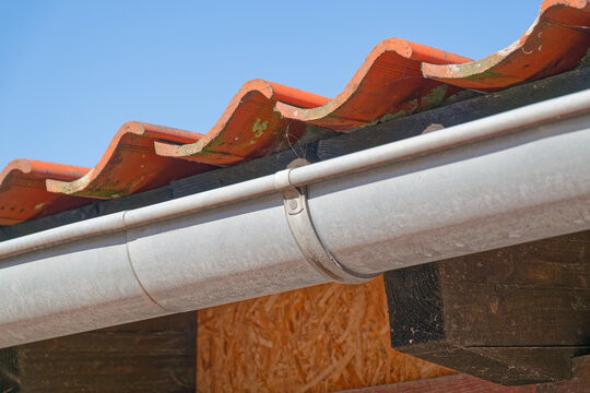 Metal rain gutter attached to roof with red clay tiles under clear blue sky