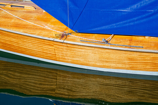 Wooden sailboat hull with blue sail and reflection on calm water surface