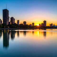 Naklejka premium Breathtaking cityscape reflecting on a serene lake during a vibrant sunset with glowing skyscrapers and a radiant sunburst. Urban skyline, travel, and architecture concept banner.