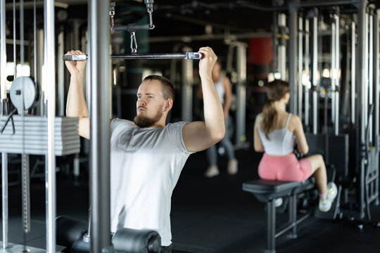 Young athletic man in sportswear training his arms muscles on machine in gym