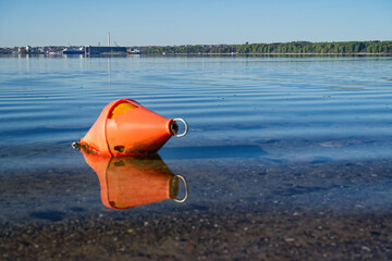 Orange buoy floating on calm water with city and forest in the background © Holger