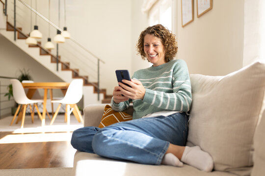 Woman laughing using smartphone on sofa at home