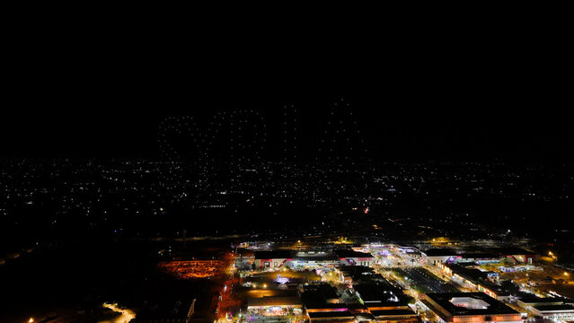 Aerial drone view of a drone light show spelling the word Syria at night. Illuminated drones forming glowing letters in the dark sky. Nighttime cityscape and glowing urban landscape.