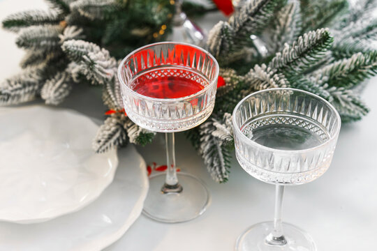 Two elegant crystal glasses and frosted evergreen arrangement on background, create an aesthetic Christmas and New Year table setting, festive spirit and warmth of winter holiday celebrations.