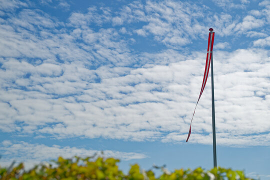 Red windsock fluttering on pole against blue sky with scattered white clouds
