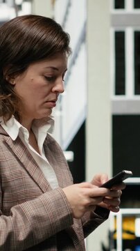 Vertical composition: Confused businesswoman checks a map app for directions on a busy downtown street, trying to find the correct route to her city destination using smartphone navigation.
