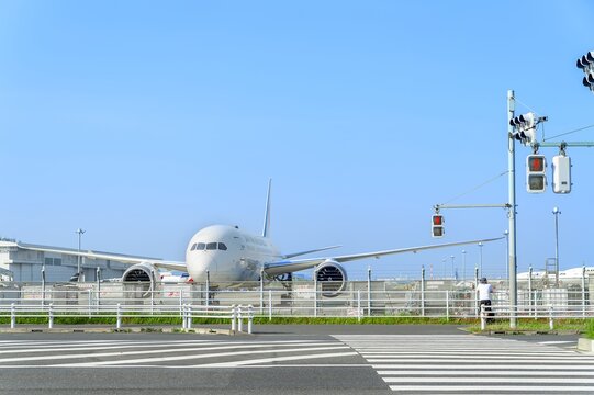 道路沿いの柵越しに見える駐機中の旅客機正面/Front View of a Parked Airliner Seen Beyond the Road Fence
