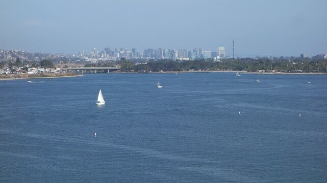 Bird-eye view of sailboats on the serene waters of Mission Bay, with the distant San Diego city skyline rising against a clear sky, coastal Southern California in summer