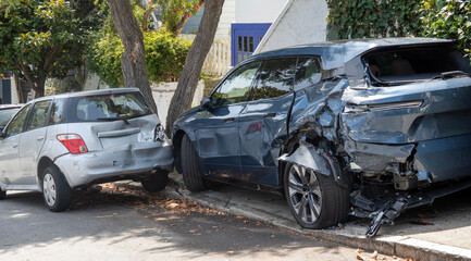 2 car hit and run damage-Two heavily damaged cars are parked on a city street next to a curb and trees after a suspected hit-and-run collision. © Noel
