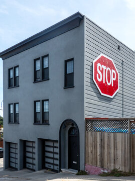 A grey multi-story building features a large red stop sign mounted on its side wall next to a wooden fence.