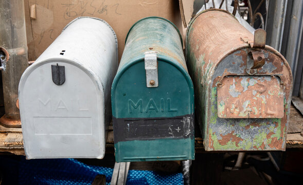 Old Mailboxes-Three weathered, vintage mailboxes in white, green, and rusty tones sit side-by-side on a wooden surface.
