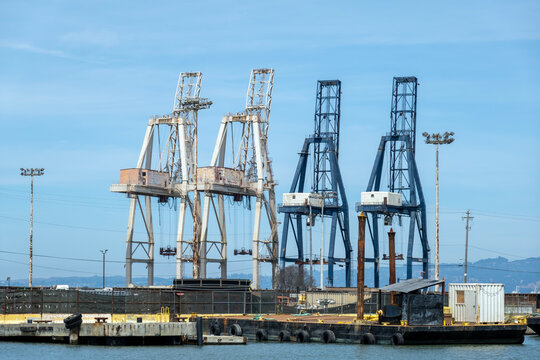Port Cranes-Large industrial shipping cranes stand tall against a clear blue sky near a concrete harbor pier.