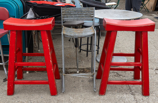 Red Stools-Two vibrant red wooden bar stools flank a weathered metal chair in aused outdoor furniture display area.