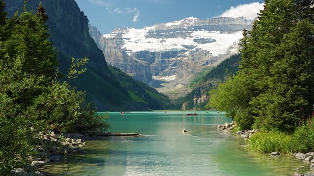 Lake Louise summer landscape with tourists canoeing on turquoise water under Victoria Glacier. Banff, Alberta, Canada.