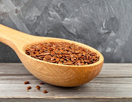 Fresh brown flaxseeds in a wooden spoon on a rustic textured surface. Ideal for healthy eating, superfood marketing, and organic nutrition concepts.