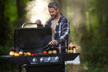 Outdoor cooking brings vegetables and meat. Outdoor cooking suits summer weekend meals. Mature man...