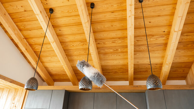 Cleaning metal pendant lamps with a microfiber duster in a modern interior with wooden ceiling. Home cleaning and interior care concept.