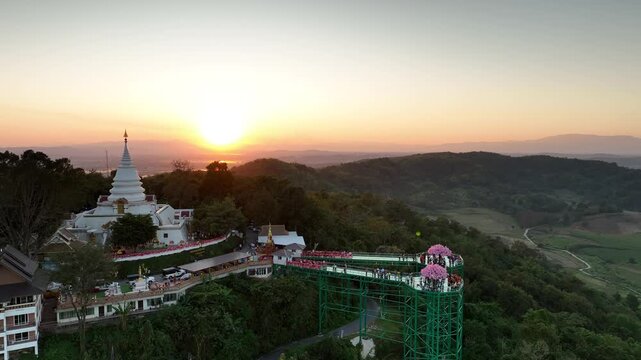 Aerial view of the skywalk and temple at sunset. The structure and pagoda stand against layered hills and a glowing horizon in year 2023