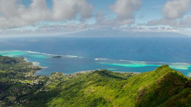 Aerial panorama of Moorea's lush green mountains and vibrant turquoise lagoon stretching towards the deep blue ocean, distant island of Tahiti creating a stunning tropical backdrop under a cloudy sky