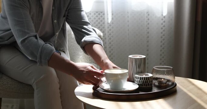 Woman taking coffee from wooden table with tray and burning candles indoors, closeup