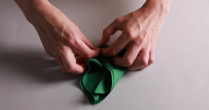 Man folding green napkin at white table indoors, closeup