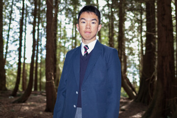 An Asian male high school student in a formal school uniform stands among trees, for graduation materials, student profiles, or education campaigns. © fotolite